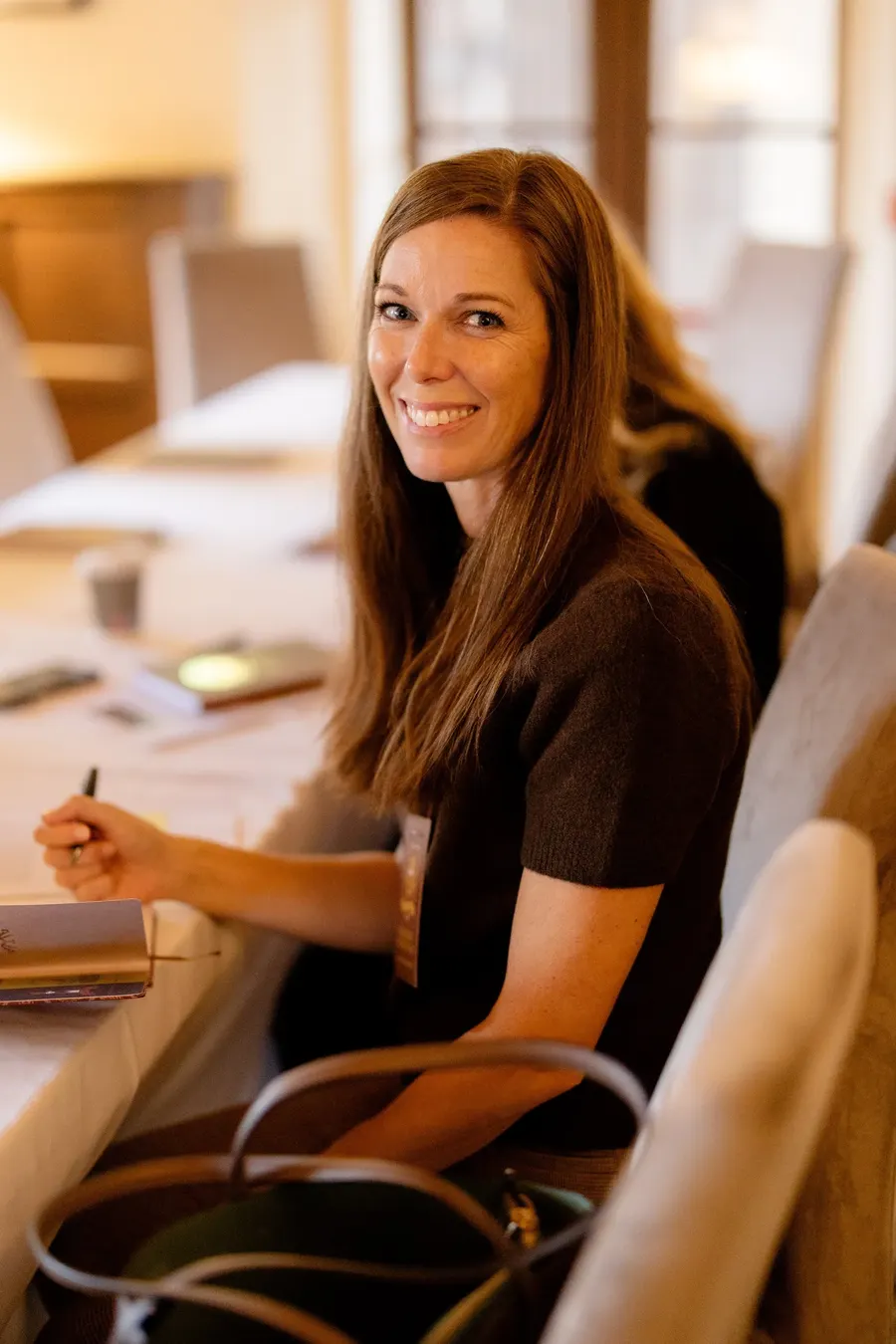 Heather O’Donovan, founder of The 185 Collective, smiling and holding a pen at a conference table in a warmly lit room